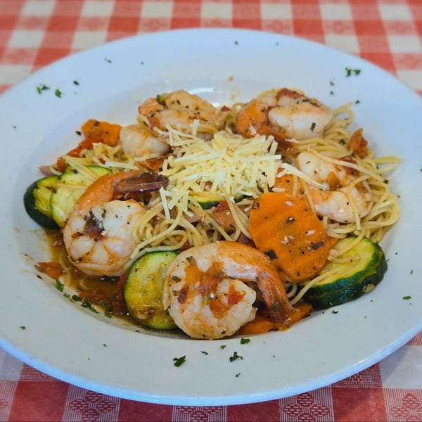 Shrimp scampi with zucchini, carrots, and shredded cheese on a white plate over a red and white checkered tablecloth.