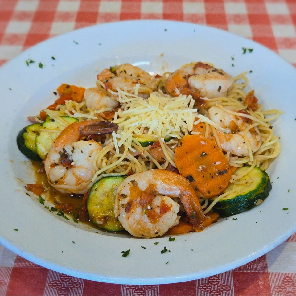 Shrimp scampi with zucchini, carrots, and shredded cheese on a white plate over a red and white checkered tablecloth.