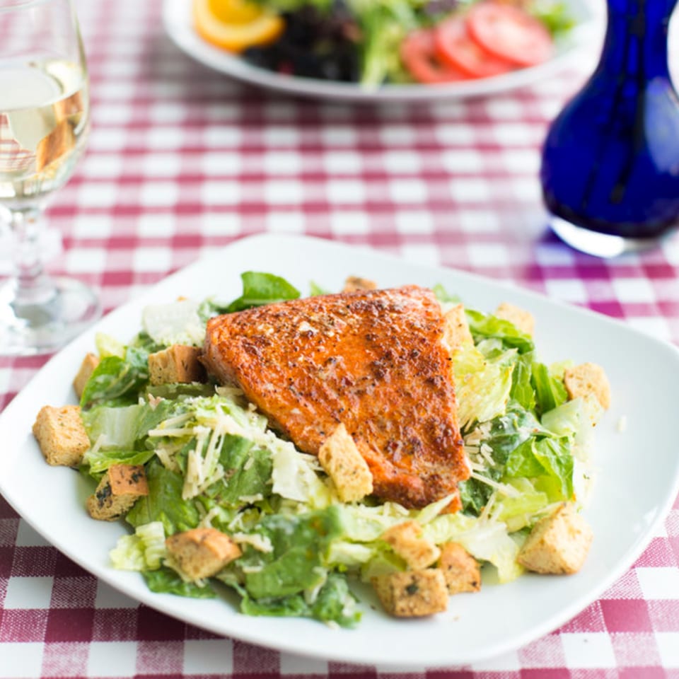 Pasta Pronto's salmon Caesar salad with croutons and white wine on a red checkered tablecloth.