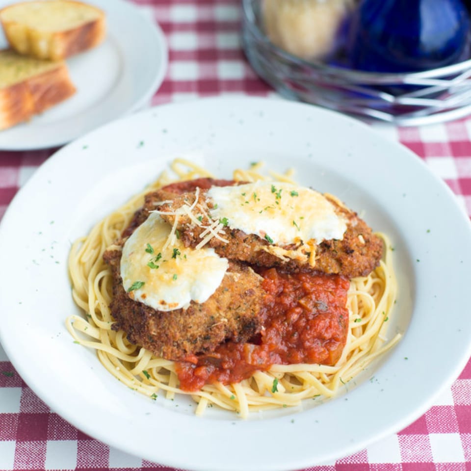 Chicken parmesan with linguine pasta and marinara sauce, topped with melted cheese and parsley.