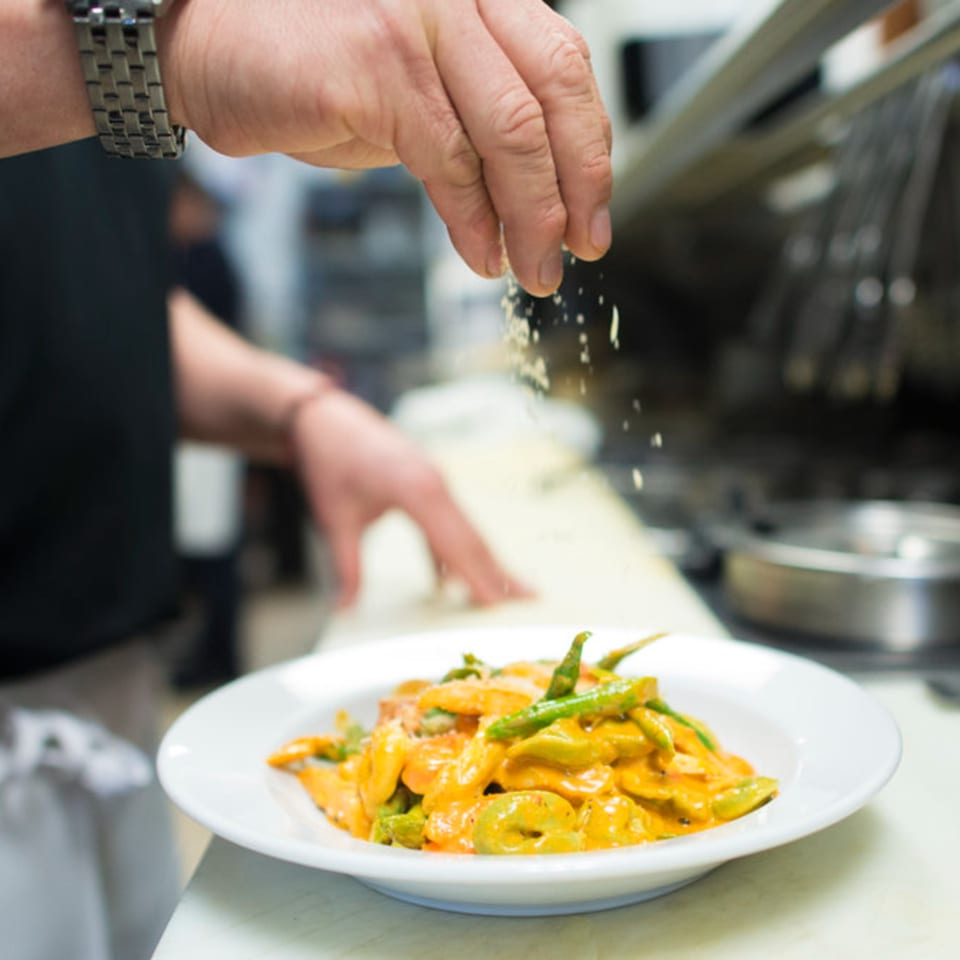 Chef's hand sprinkling parmesan cheese over a plate of Pasta Pronto's tortellini with asparagus.