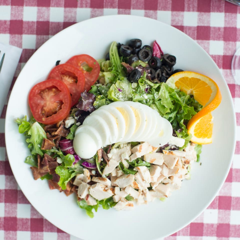 A vibrant Pasta Pronto salad with chicken, bacon, tomatoes, olives, egg, and orange slices.