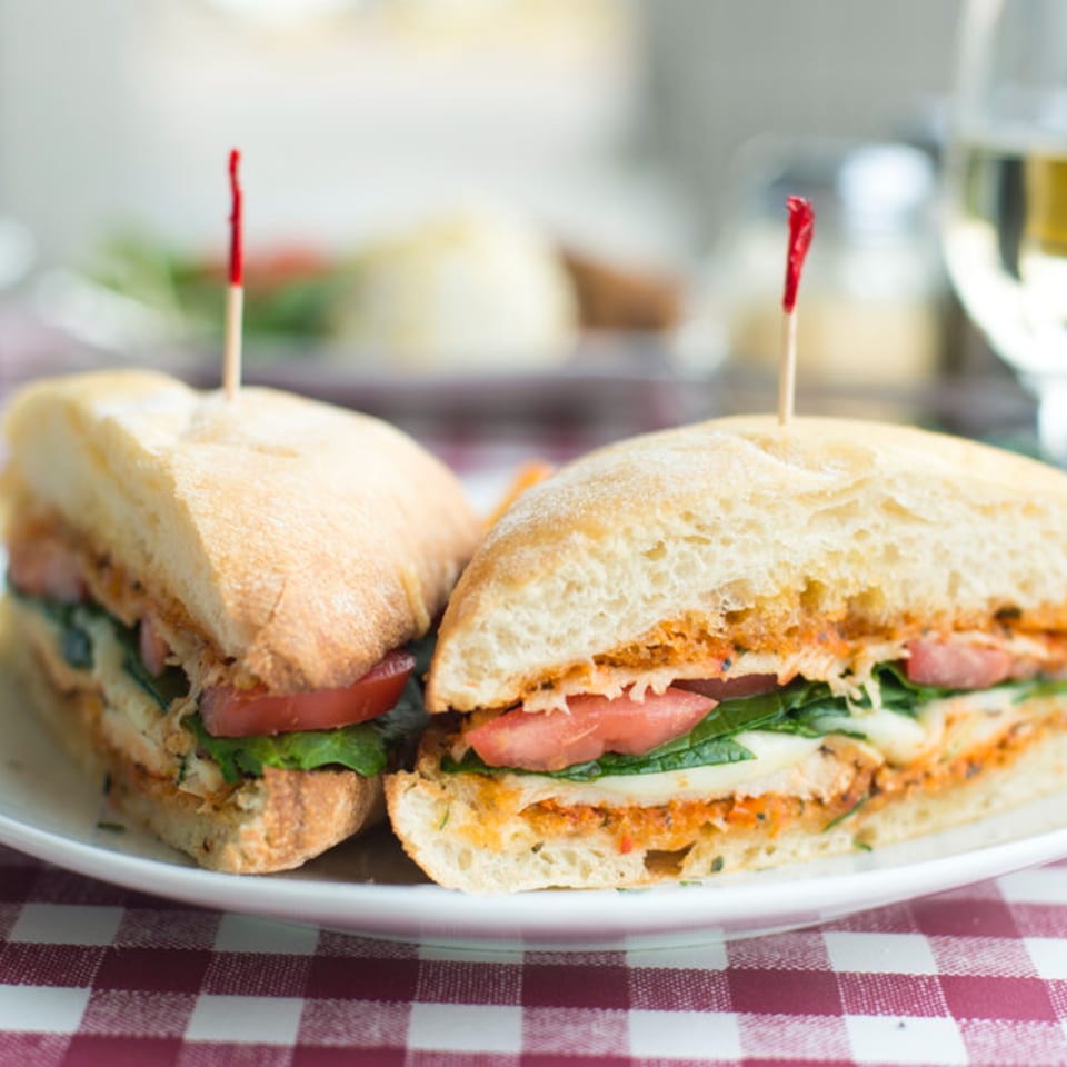 Two halves of an Italian sandwich with chicken, tomatoes, and spinach on a white plate.